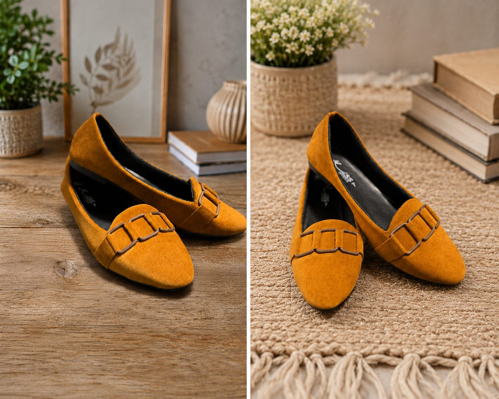 A pair of mustard yellow suede loafers with decorative buckle straps, shown in two styled indoor settings on a wooden table and a woven rug with plants and books.