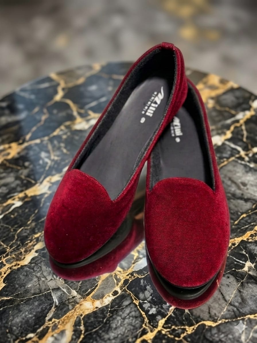 A pair of deep burgundy velvet slip on shoes with platform soles, displayed on a black and gold marble surface.